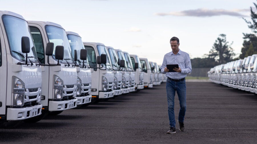 A fleet manager walks through a company lot, looking at data on a tablet